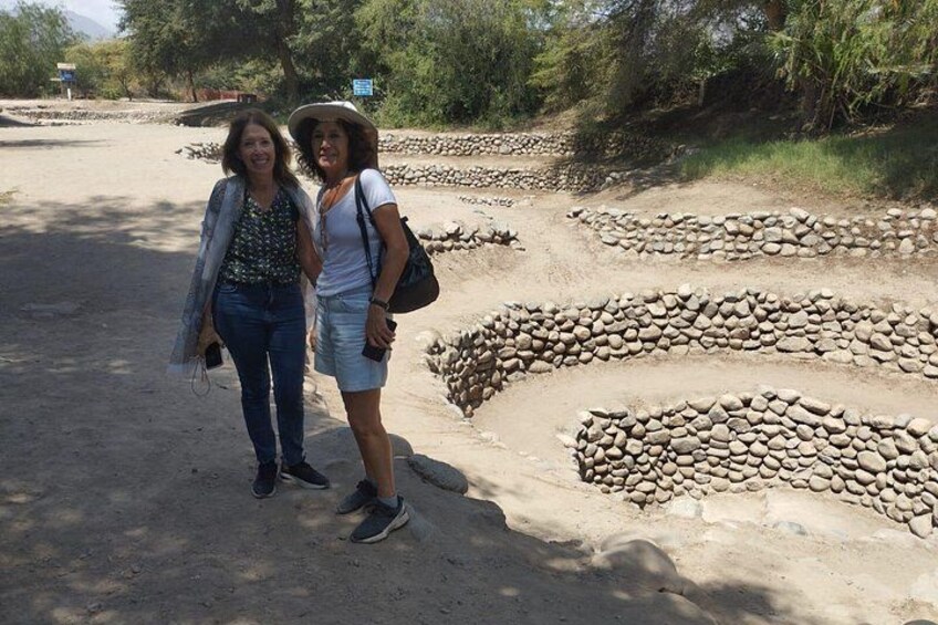 Two people standing in front of a dry riverbed with layered stone formations. 5