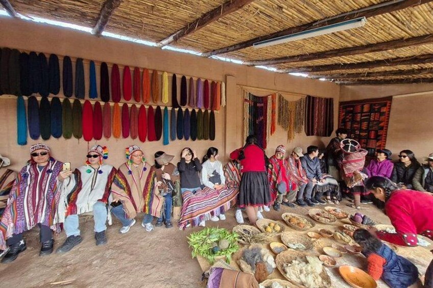 A group of people in traditional attire, a thatched roof structure, and various textiles on display. 4