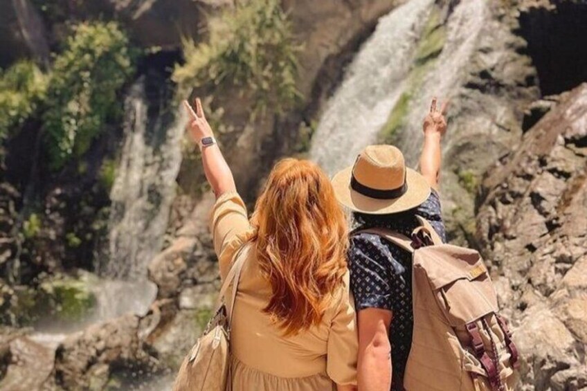Two people standing in front of a waterfall, both raising their hands. 2