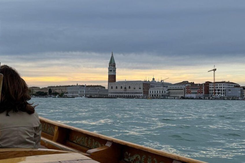 A gondola on water with a historic building and a tower in the background. 5