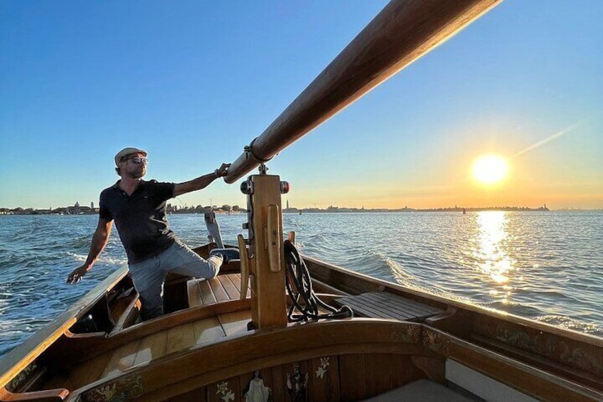 A person steering a wooden boat on a calm body of water during sunset. 1
