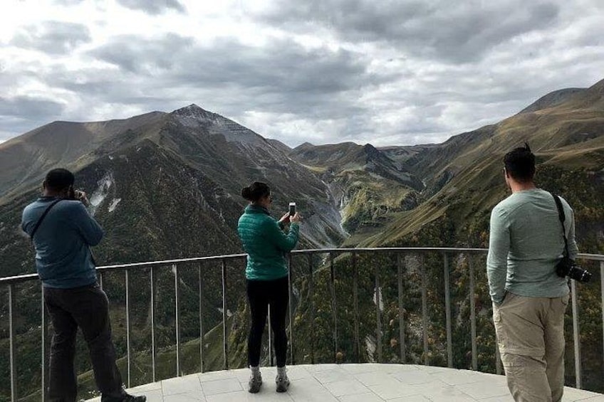 Drei Personen machen Fotos von einer Berglandschaft von einer Aussichtsplattform aus. 4