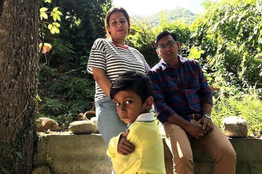 Eine Familie mit drei Personen draußen, mit einem Baum und Grünpflanzen im Hintergrund. 5