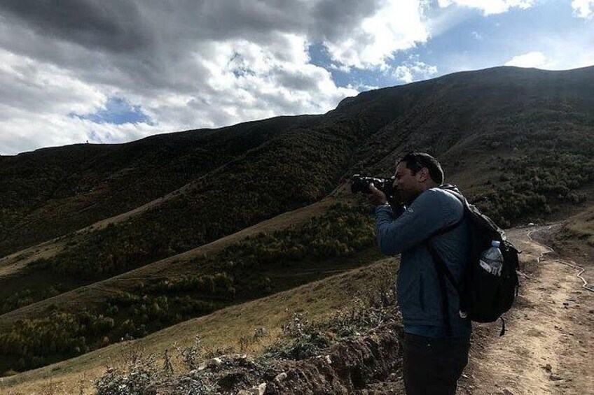 Eine Person fotografiert mit einer Kamera eine hügelige Landschaft. 3