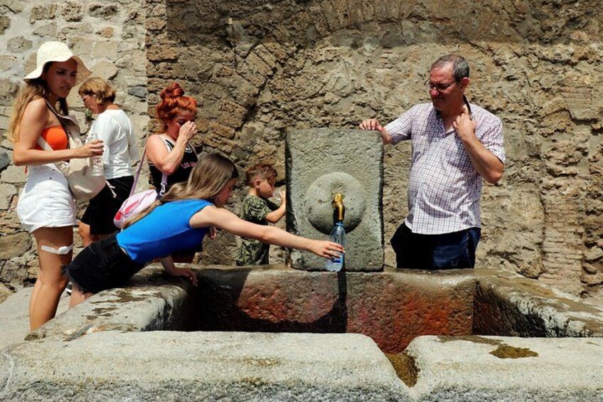 A group of people at an ancient stone well with a water spout. 4