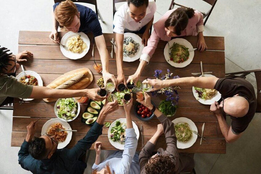 A group of people around a wooden table with various dishes, including salads, bread, and drinks. 1