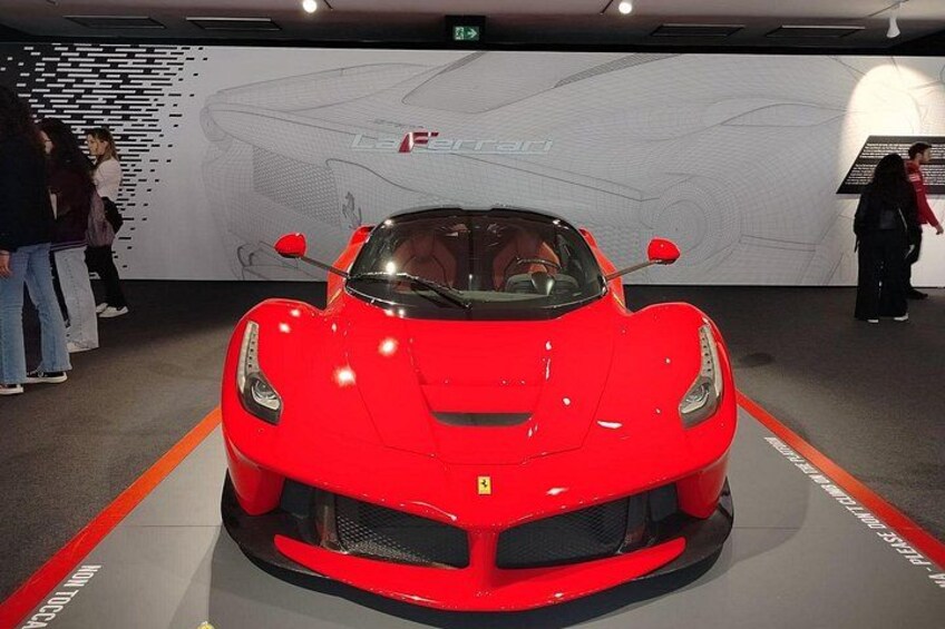 A red sports car on display with a large wall in the background. 1