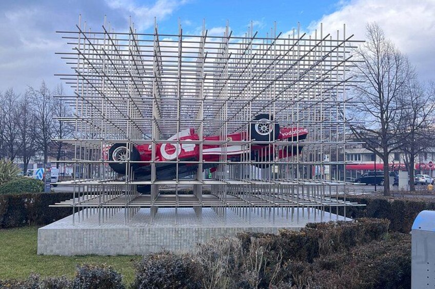 A red car suspended in a metal framework with a Vodafone building in the background. 5