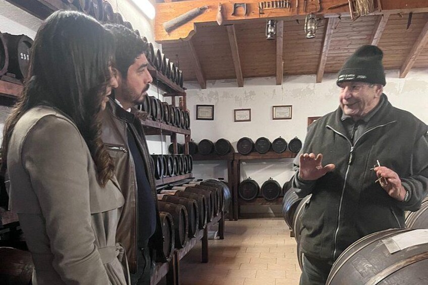 A person in a green jacket and beanie, gesturing while speaking to two others in a room with shelves of cookware. 4