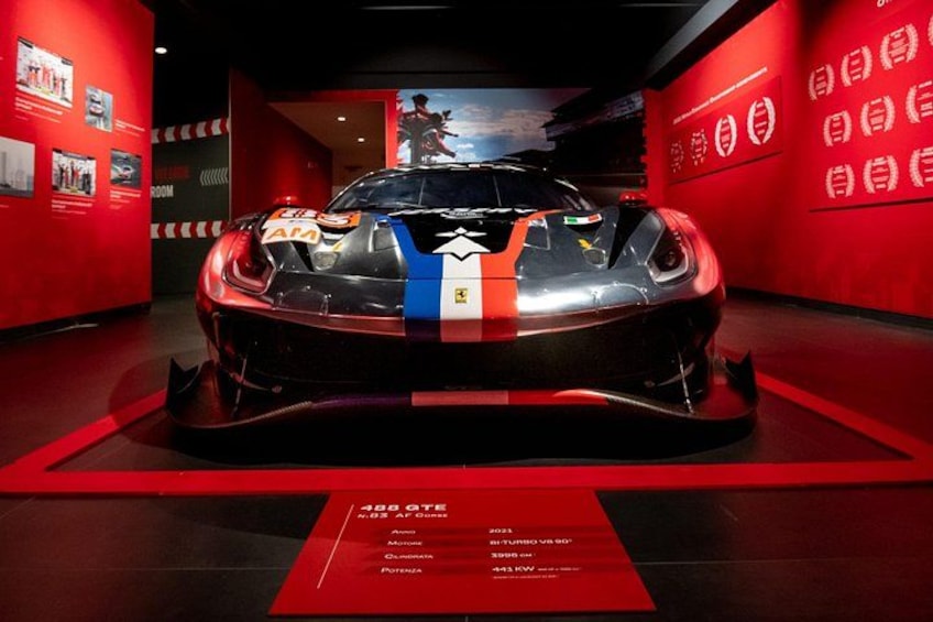 A sports car on display with a red and blue stripe, surrounded by red walls and a red floor. 3