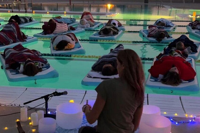 People lying on mats in a pool, possibly for a relaxation or therapy session. 3