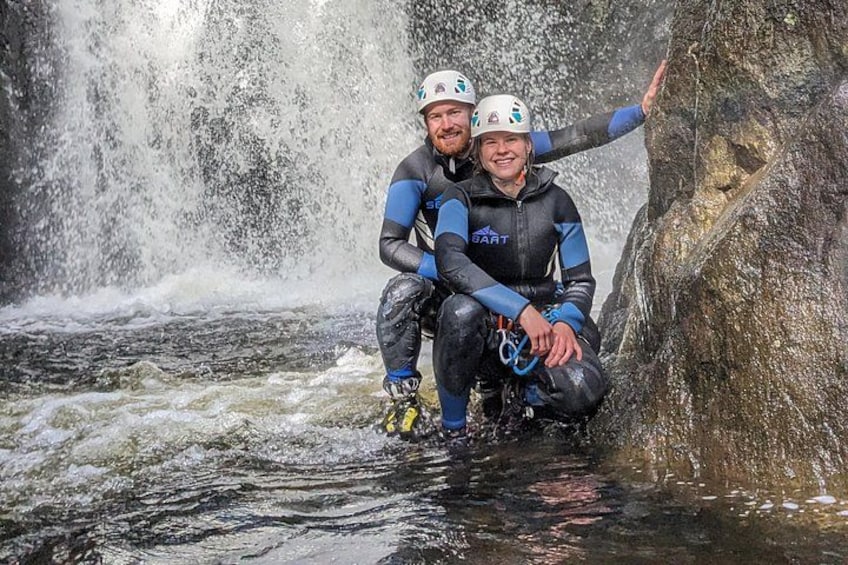 Two people in wetsuits near a waterfall. 3