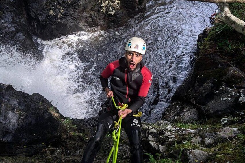 A person rappelling down a rocky cliff with a waterfall in the background. 1