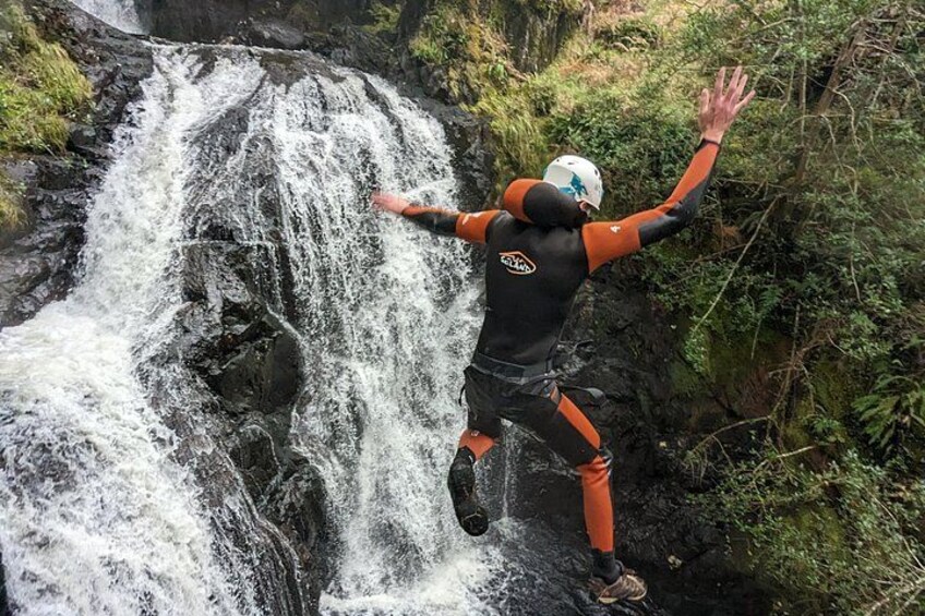 A person jumping off a waterfall in a forested area. 4