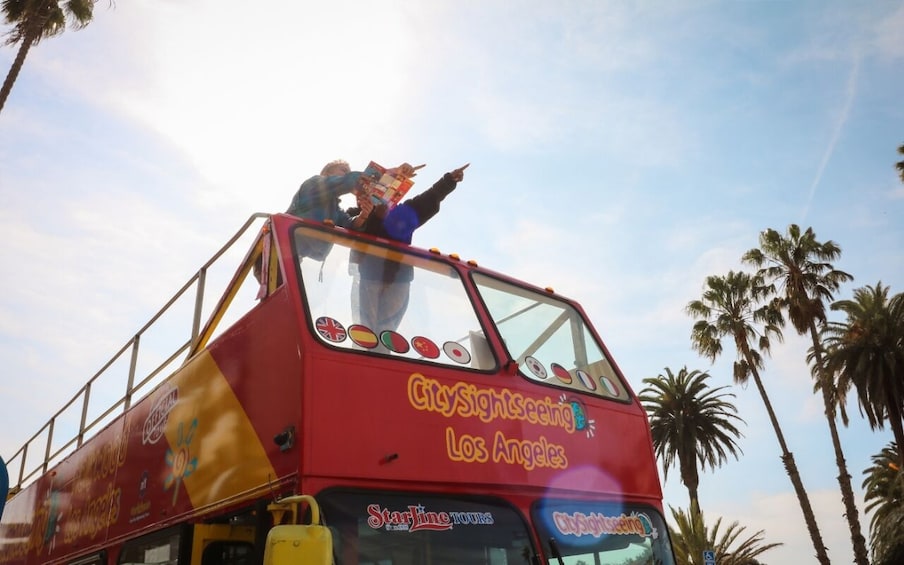 Punainen, kaksikerroksinen bussi, jonka kylkeen on maalattu teksti ”CitySightseeing Los Angeles”, on pysäköitynä, ja taustalla näkyy palmuja. 4