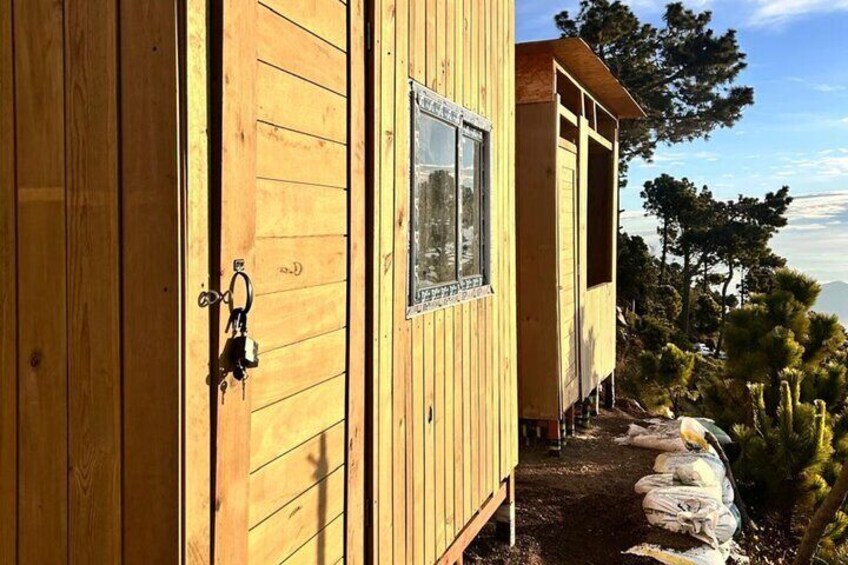 Una cabaña de madera con ventana y puerta, rodeada de árboles y un cielo despejado. 4