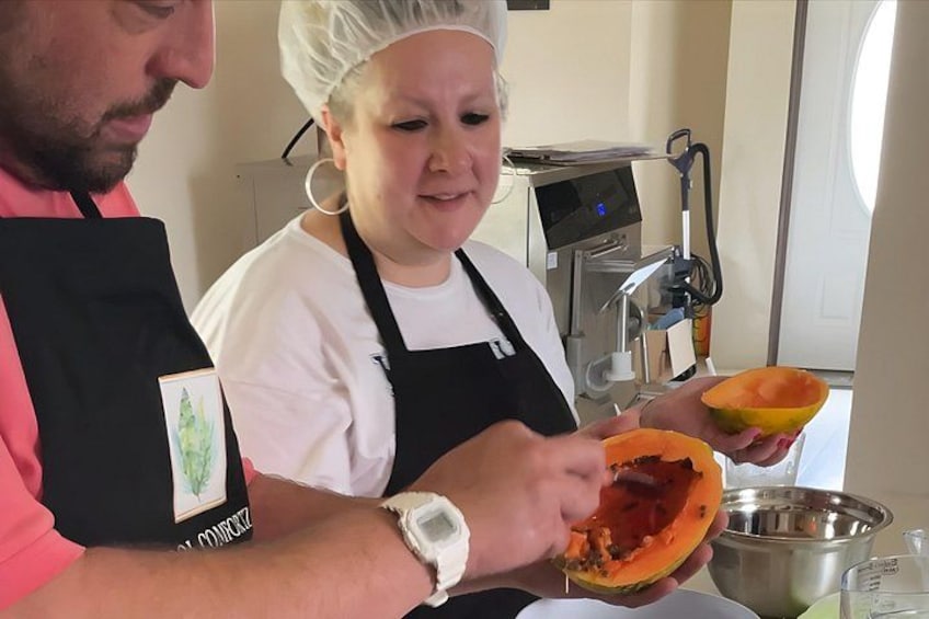 En person i hvid kokkejakke og hårnet holder en halveret papaya. 1
