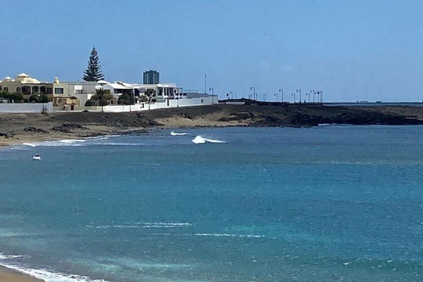A beach with clear blue water, a white boat, and buildings in the background. 4