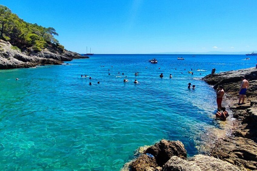 A coastal scene with clear turquoise water, rocky shorelines, and people swimming and standing on the rocks. 5