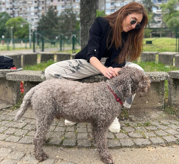 A person sitting on a stone bench with a curly-haired dog. 4