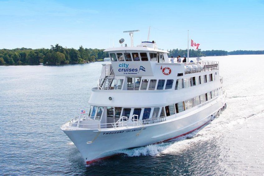 Un navire de croisière blanc, sur lequel on peut lire les mots « city cruises » sur le côté, navigue sur une étendue d’eau, avec une côte boisée en arrière-plan. 2