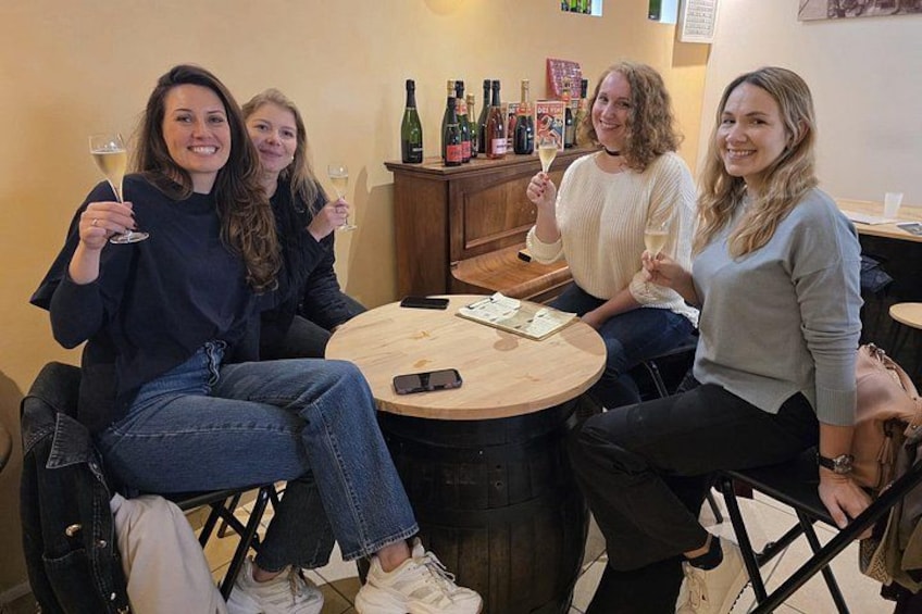 Vier Personen sitzen an einem runden Tisch, Wein gläser, eine Speisekarte und Weinflaschen sind im Hintergrund zu sehen. 5