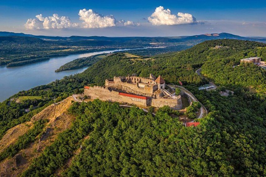 Un castillo en una colina con vista a un río, rodeado de bosque denso. 1