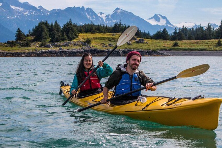 Dos personas remando en kayak en un lago tranquilo, con montañas al fondo. 2
