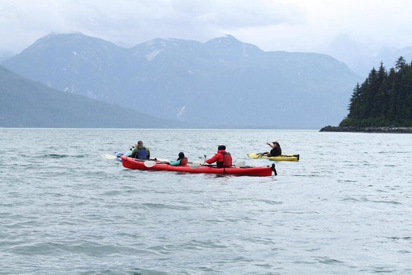 Tres personas kayakendo en un lago tranquilo con montañas al fondo. 4
