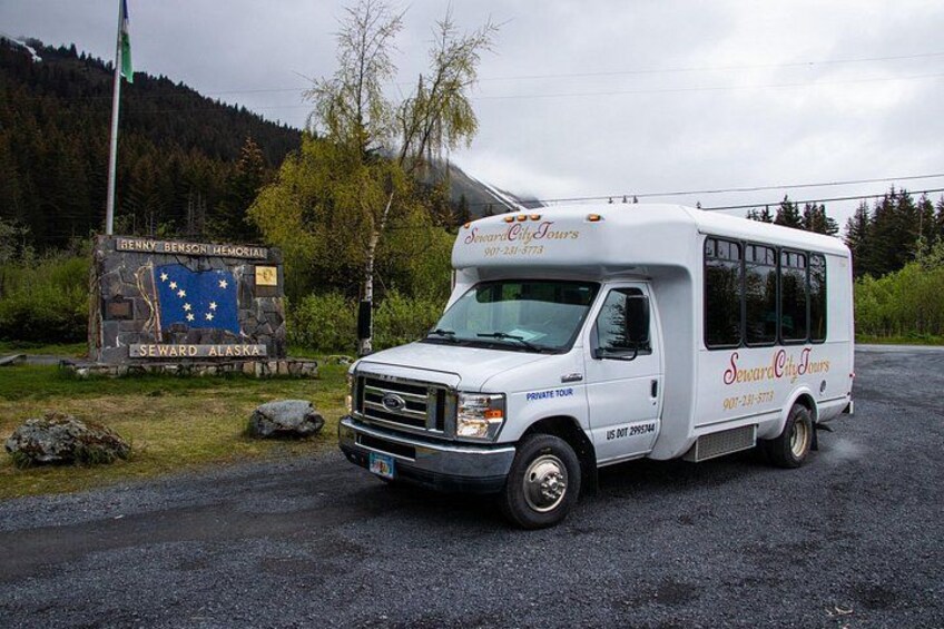 A white tour bus parked near a sign with a flag and text. 3
