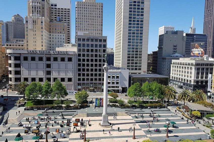 A city square with a monument, buildings, and trees. 4