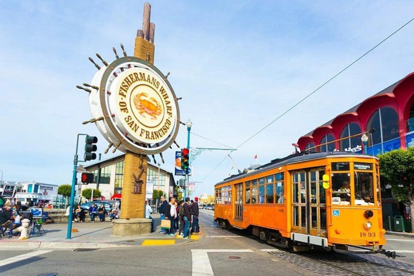 A streetcar at a crosswalk with a large sign reading '10 Fisherman's Wharf San Francisco.' 5