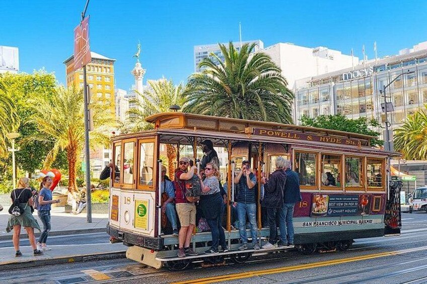 A cable car with passengers, a palm tree, and a building in the background. 2