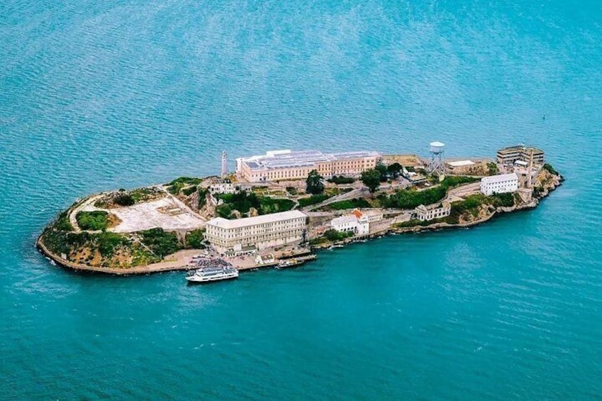 An aerial view of a coastal island with buildings, a lighthouse, and a boat docked near the shore. 1