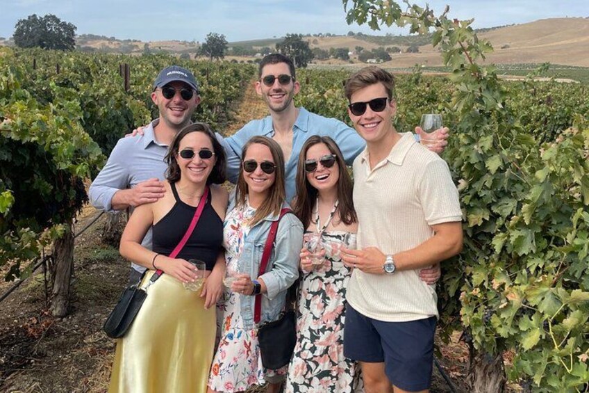 A group of people in a vineyard with rows of grapevines. 4