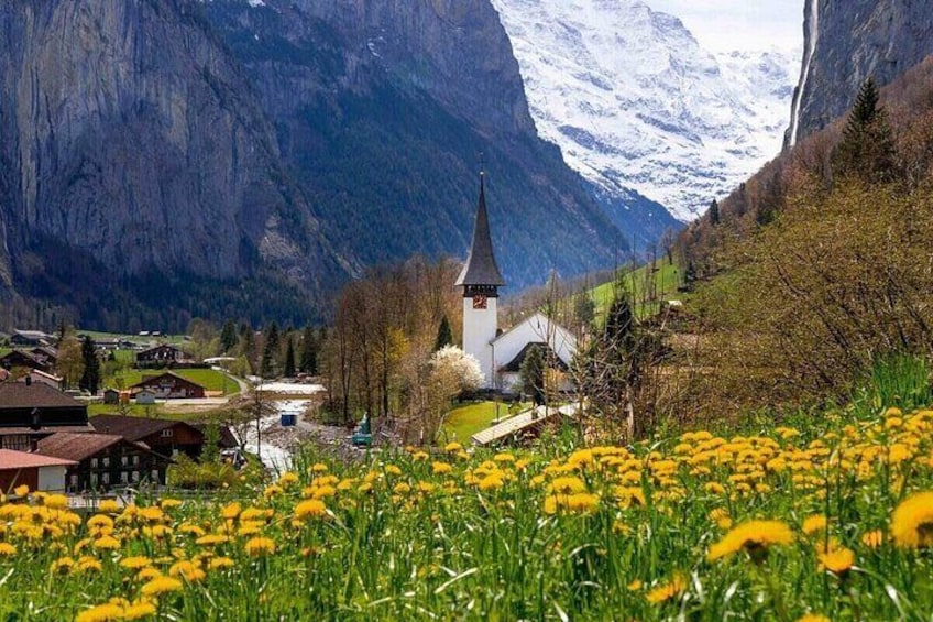 Un pueblo con una iglesia, montañas y un campo de flores amarillas. 1