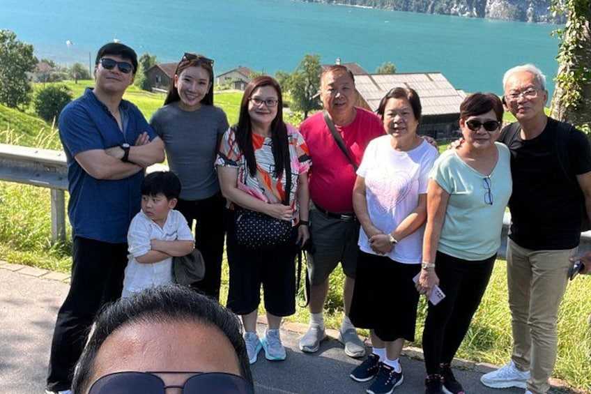 Un grupo de personas de pie junto a una carretera con un lago al fondo. 4