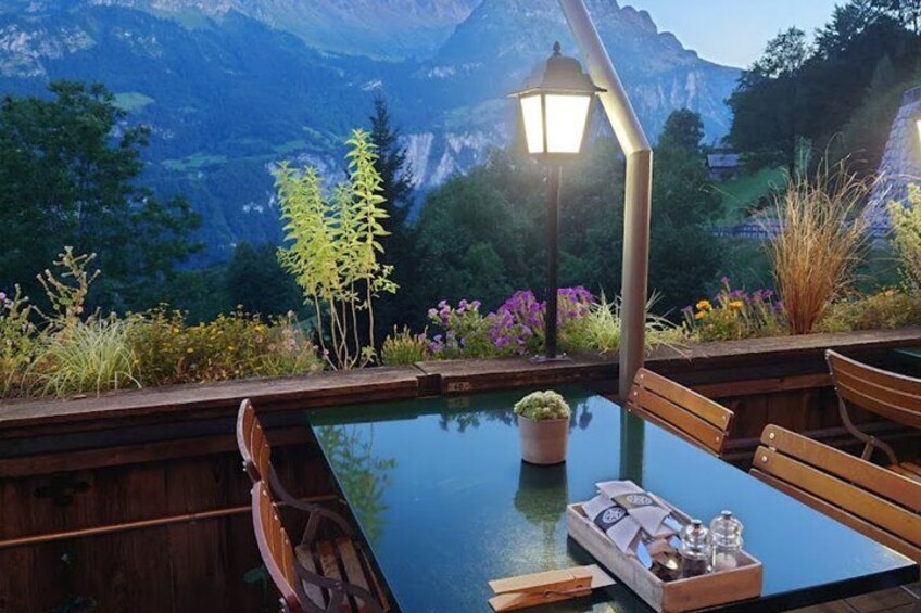 Una terraza de madera con una mesa de vidrio, sillas y una planta en maceta. 2