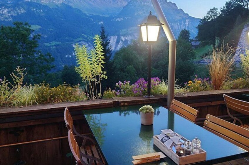 Eine Holzterrasse mit einem Glastisch, umgeben von Stühlen und einem Lampenpfosten. 2