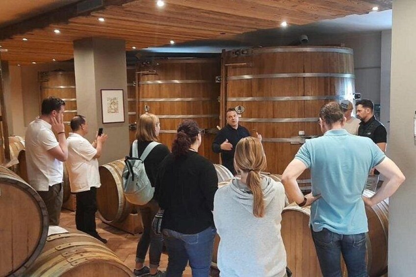 A group of people inside a wine cellar with wooden barrels. 5