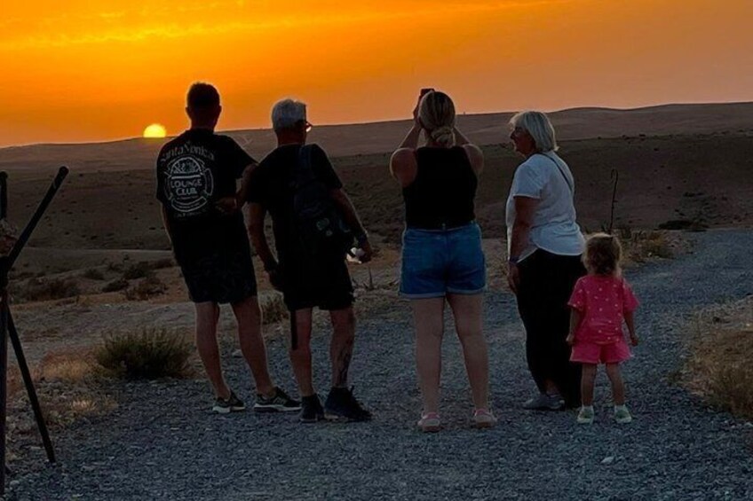 Un grupo de personas de pie sobre un sendero de grava al atardecer. 2