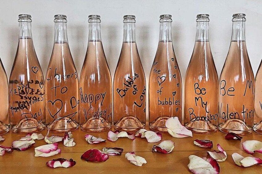 A row of glass bottles with handwritten messages, surrounded by scattered flower petals. 5