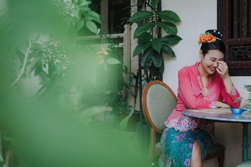 A person sitting at a table with a blue bowl, surrounded by greenery and a wooden chair. 2