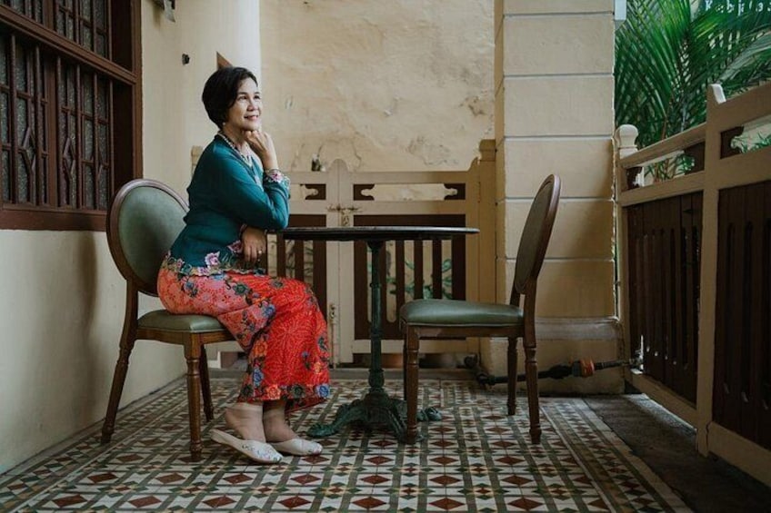 A person sitting on a chair in a room with patterned flooring, a wooden table, and a railing. 1
