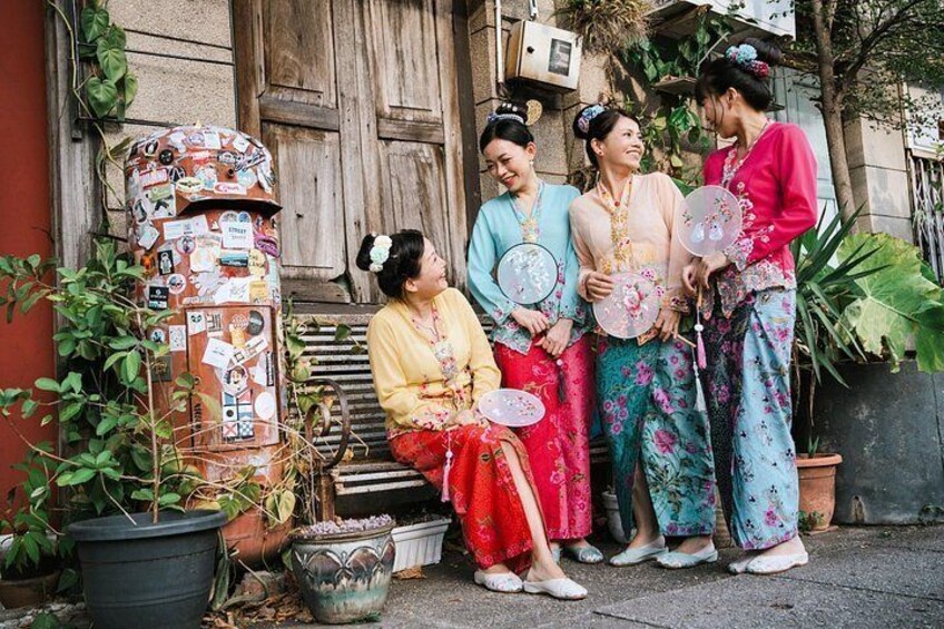A group of people in traditional attire standing in front of a rustic building with a wooden door and potted plants. 3