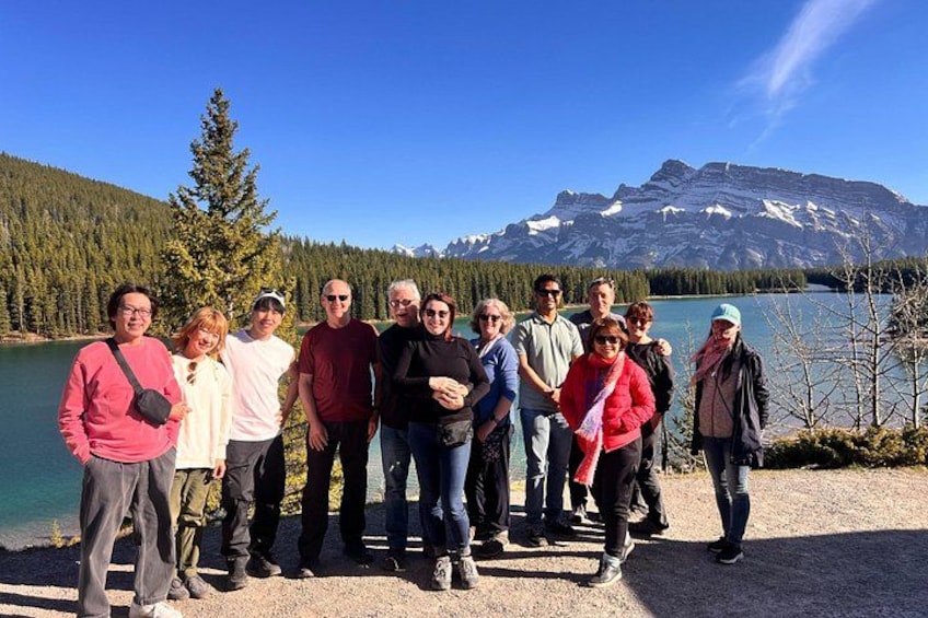 Un grupo de personas de pie junto a un lago, con montañas al fondo. 3
