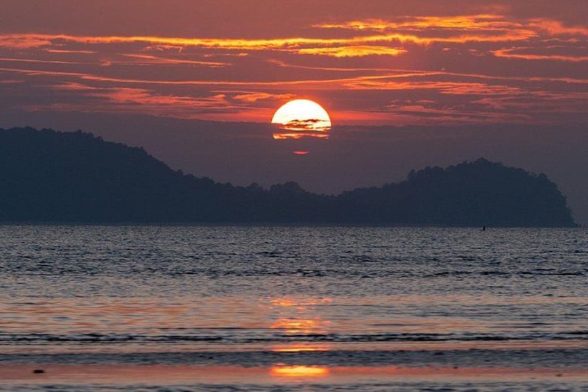 Een zonsondergang boven een wateroppervlak met een donkere contourover van land in de verte. 2