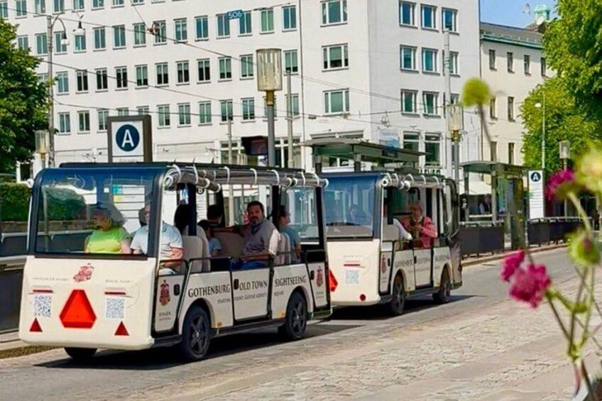 Een dubbeldekkerbus met passagiers, een bushalte en een gebouw met veel ramen op de achtergrond. 3