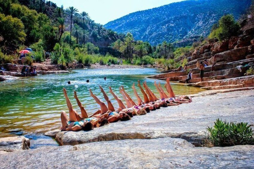 A river with people relaxing on rocks, a clear sky, and a mountainous backdrop. 1