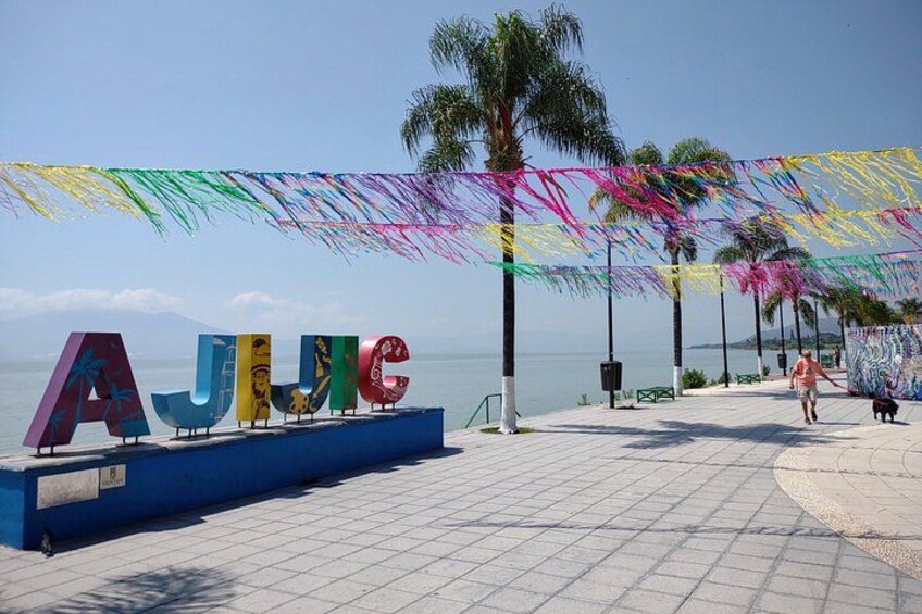 A beach with colorful letters spelling 'AJUC' on a blue platform, palm trees, and a clear sky. 2